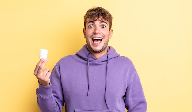 Hombre guapo joven que parece feliz y gratamente sorprendido. concepto de botella de pastillas