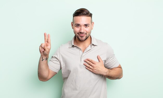 Hombre guapo joven que parece feliz, seguro y digno de confianza, sonriendo y mostrando el signo de la victoria, con una actitud positiva