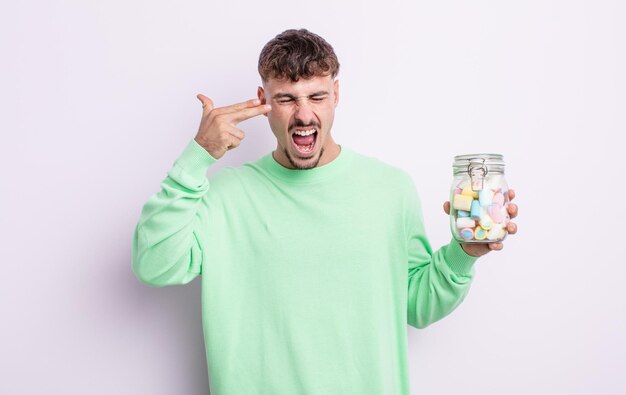 Hombre guapo joven que parece infeliz y estresado, gesto suicida haciendo señas de armas. concepto de caramelos de gelatina