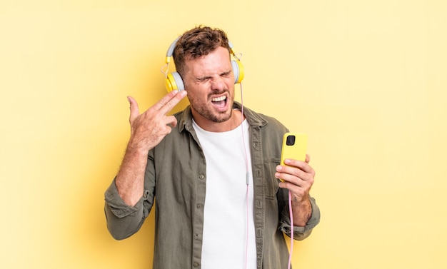 Hombre guapo joven que parece infeliz y estresado, gesto de suicidio haciendo auriculares con señal de pistola y concepto de teléfono inteligente