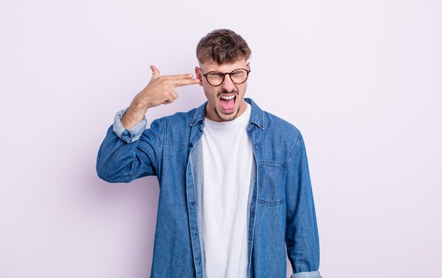 Hombre guapo joven que parece infeliz y estresado gesto de suicidio haciendo señal de pistola con la mano apuntando a la cabeza