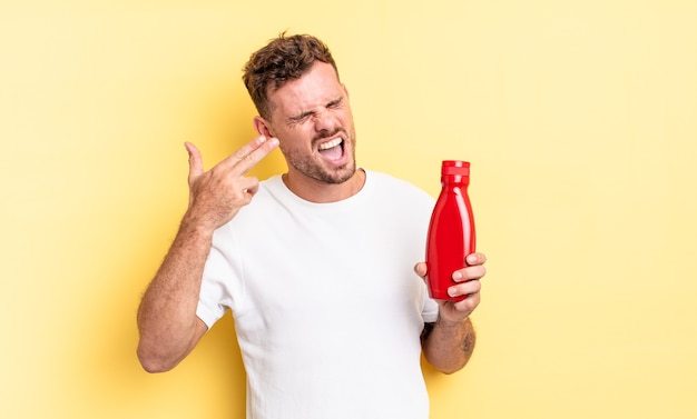 Hombre guapo joven que parece infeliz y estresado, gesto de suicidio haciendo signo de pistola. concepto de salsa de tomate