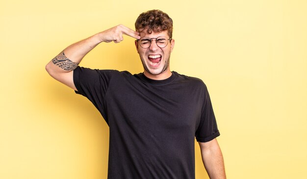 Hombre guapo joven que parece infeliz y estresado, gesto de suicidio haciendo un signo de pistola con la mano, apuntando a la cabeza