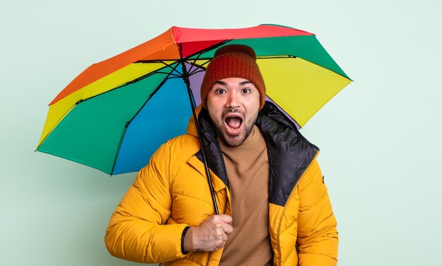 Hombre guapo joven que parece muy conmocionado o sorprendido. concepto de lluvia y paraguas