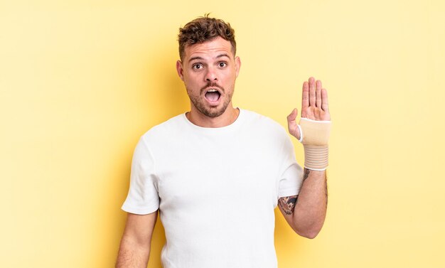 Hombre guapo joven que parece muy conmocionado o sorprendido. concepto de vendaje de mano