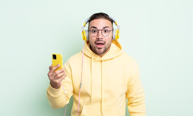 Hombre guapo joven que parece muy sorprendido o sorprendido. auriculares y concepto de teléfono inteligente