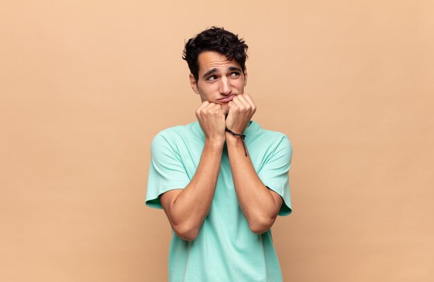 Hombre guapo joven que parece preocupado, ansioso, estresado y asustado, mordiéndose las uñas y mirando al espacio de copia lateral