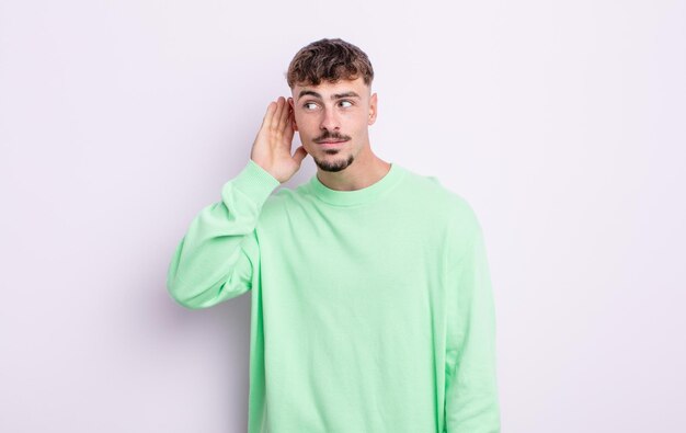 Hombre guapo joven que parece serio y curioso, escuchando, tratando de escuchar una conversación secreta o chismes, escuchando a escondidas