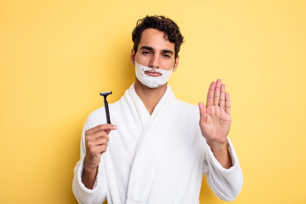 Hombre guapo joven que parece serio mostrando la palma abierta haciendo gesto de parada. concepto de afeitado y espuma