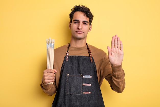 Hombre guapo joven que parece serio mostrando la palma abierta haciendo gesto de parada. concepto de artista