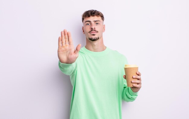 Hombre guapo joven que parece serio mostrando la palma abierta haciendo gesto de parada. concepto de café para llevar