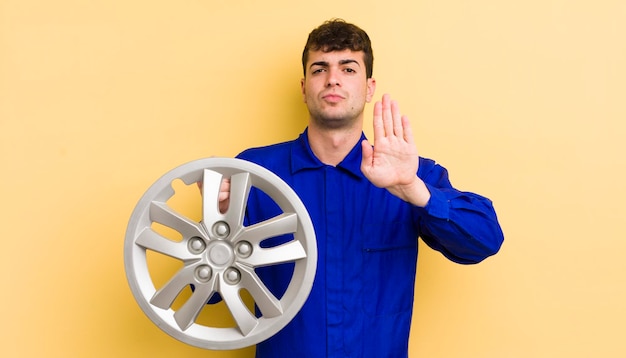 Hombre guapo joven que parece serio mostrando la palma abierta haciendo gesto de parada concepto de reparador de automóviles