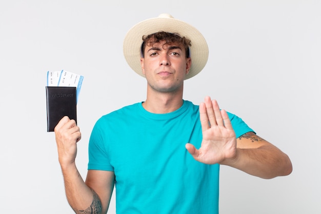 Hombre guapo joven que parece serio mostrando la palma abierta haciendo gesto de parada. viajero sosteniendo su pasaporte