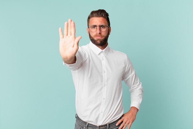 Hombre guapo joven que parece serio mostrando la palma abierta haciendo gesto de parada