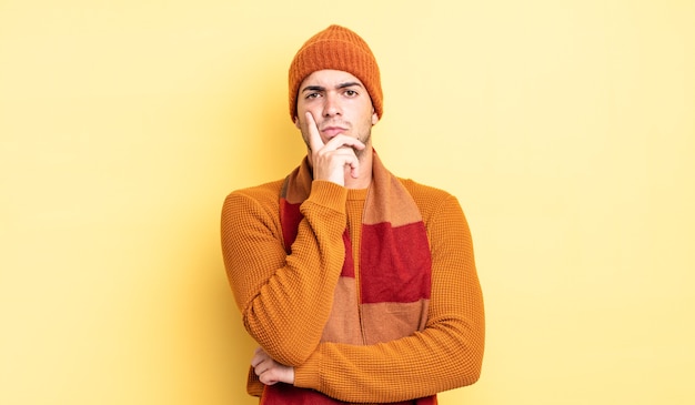 Hombre guapo joven que parece serio, pensativo y desconfiado, con un brazo cruzado y la mano en la barbilla, opciones de ponderación