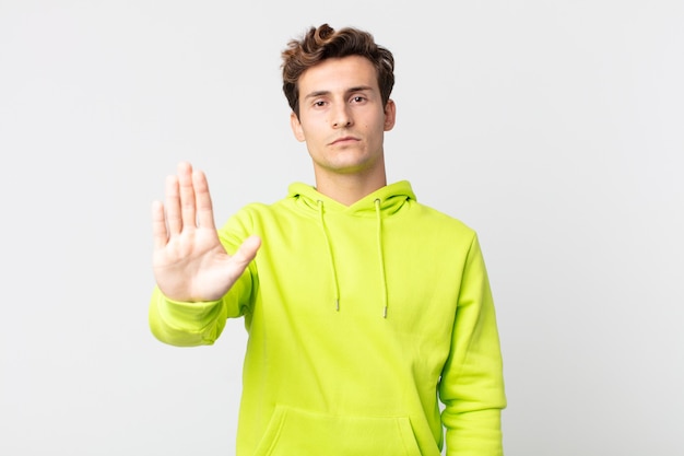 Hombre guapo joven que parece serio, severo, disgustado y enojado mostrando la palma abierta haciendo gesto de parada