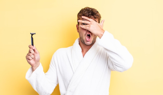 Hombre guapo joven que parece sorprendido, asustado o aterrorizado, cubriendo la cara con la mano. concepto de afeitado