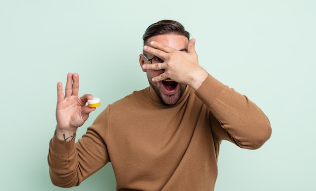 Hombre guapo joven que parece sorprendido, asustado o aterrorizado, cubriendo el rostro con la mano. lentes de contacto