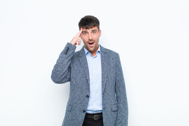 Hombre guapo joven que parece sorprendido, con la boca abierta, conmocionado, dándose cuenta de un nuevo pensamiento, idea o concepto sobre la pared blanca