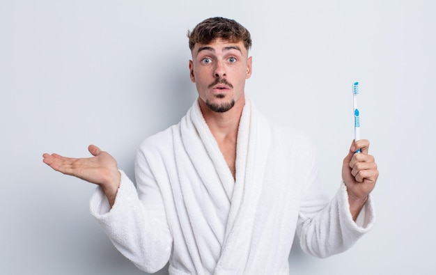 Hombre guapo joven que parece sorprendido y conmocionado con la mandíbula caída sosteniendo un concepto de cepillo de dientes de objeto