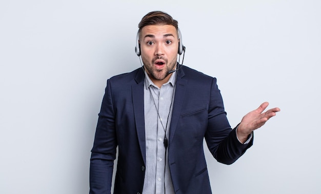 Hombre guapo joven que parece sorprendido y conmocionado con la mandíbula caída sosteniendo un concepto de objeto telearketer