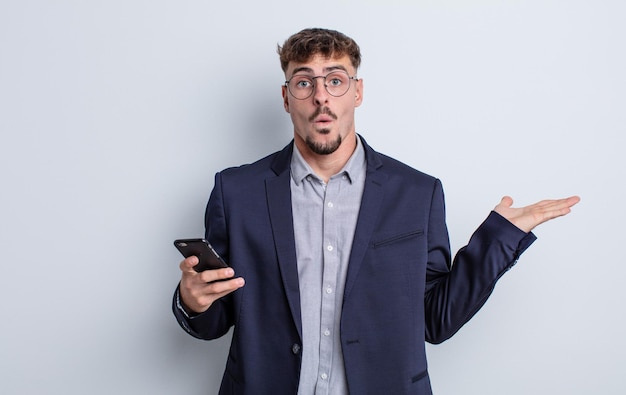 Hombre guapo joven que parece sorprendido y conmocionado, con la mandíbula caída sosteniendo un objeto. concepto de negocio