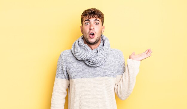 Hombre guapo joven que parece sorprendido y conmocionado, con la mandíbula caída sosteniendo un objeto con una mano abierta en el costado