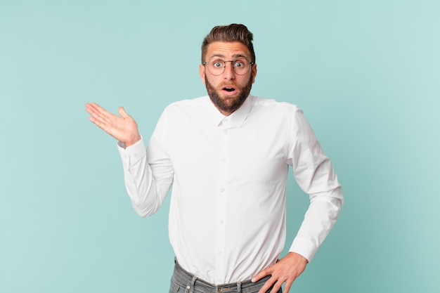 Hombre guapo joven que parece sorprendido y conmocionado, con la mandíbula caída sosteniendo un objeto