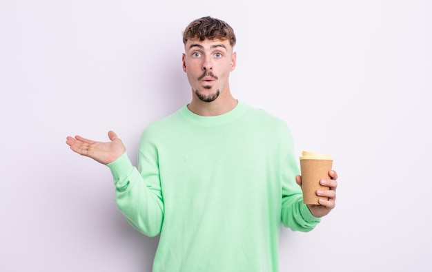 Hombre guapo joven que parece sorprendido y consternado, con la mandíbula caída sosteniendo un objeto. concepto de café para llevar