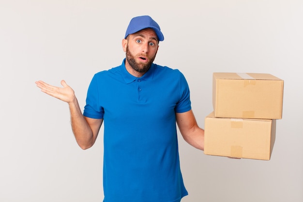 Hombre guapo joven que parece sorprendido y consternado, con la mandíbula caída sosteniendo un objeto. concepto de entrega de paquetes