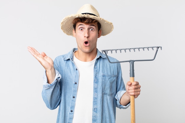 Hombre guapo joven que parece sorprendido y consternado, con la mandíbula caída sosteniendo un objeto. concepto de granjero