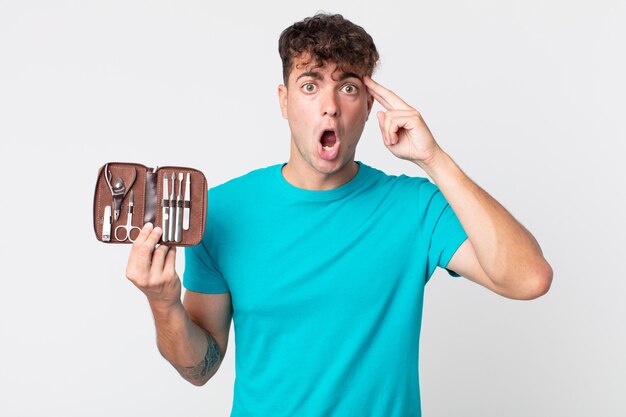 Hombre guapo joven que parece sorprendido, dándose cuenta de un nuevo pensamiento, idea o concepto y sosteniendo una caja de herramientas de uñas