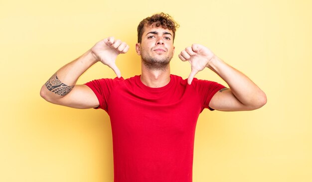 Hombre guapo joven que parece triste, decepcionado o enojado, mostrando los pulgares hacia abajo en desacuerdo, sintiéndose frustrado