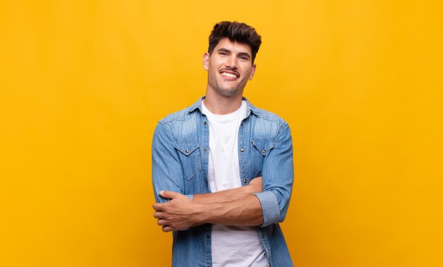 Hombre guapo joven que parece un triunfador feliz, orgulloso y satisfecho sonriendo con los brazos cruzados