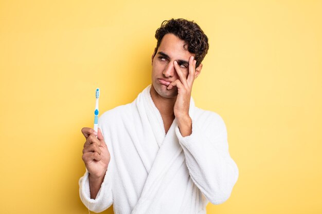 Hombre guapo joven que se siente aburrido, frustrado y con sueño después de un cansancio. concepto de albornoz y cepillo de dientes