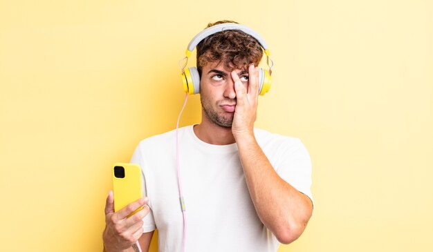 Hombre guapo joven que se siente aburrido, frustrado y con sueño después de un cansancio. concepto de auriculares y teléfono inteligente