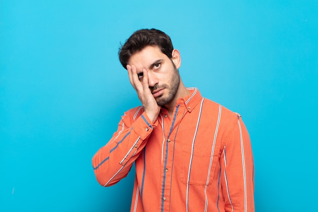 Hombre guapo joven que se siente aburrido, frustrado y con sueño después de una tarea tediosa, aburrida y tediosa, sosteniendo la cara con la mano