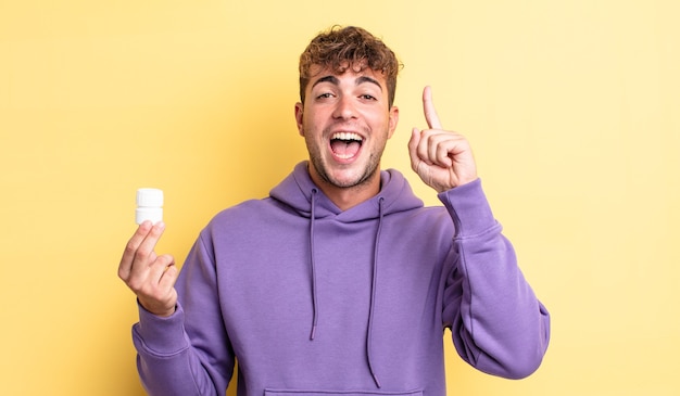 Hombre guapo joven que se siente como un genio feliz y emocionado después de darse cuenta de una idea. concepto de botella de pastillas