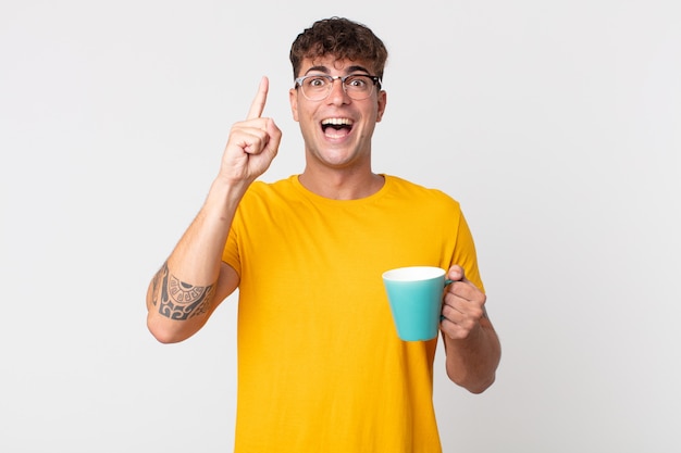 Hombre guapo joven que se siente como un genio feliz y emocionado después de darse cuenta de una idea y sostener una taza de café