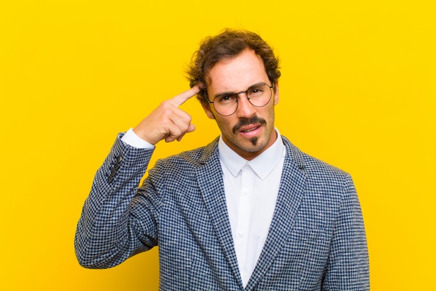 Hombre guapo joven que se siente confundido y perplejo, mostrando que estás loco, loco o loco en la pared naranja