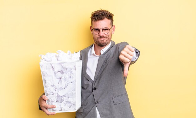 Hombre guapo joven que se siente cruzado, mostrando los pulgares hacia abajo concepto de basura de bolas de papel