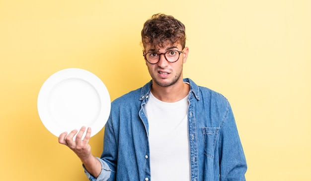 Hombre guapo joven que se siente desconcertado y confundido. concepto de plato vacío