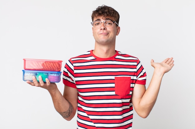 Hombre guapo joven que se siente desconcertado y confundido y dudando y sosteniendo una lonchera