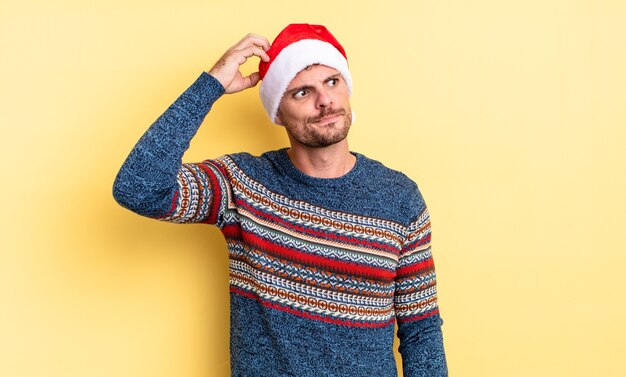 Hombre guapo joven que se siente desconcertado y confundido, rascándose la cabeza. concepto de navidad