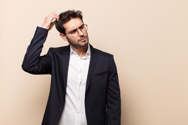 Hombre guapo joven que se siente desconcertado y confundido, rascándose la cabeza y mirando hacia un lado