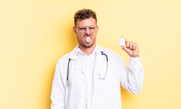 Hombre guapo joven que se siente disgustado e irritado y con la lengua fuera. concepto de botella de píldoras médico