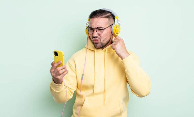 Hombre guapo joven que se siente estresado, ansioso, cansado y frustrado. auriculares y concepto de teléfono inteligente