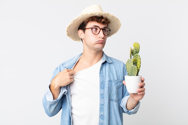 Hombre guapo joven que se siente estresado, ansioso, cansado y frustrado. granjero sosteniendo un cactus decorativo