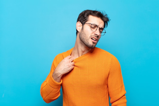 Hombre guapo joven que se siente estresado, ansioso, cansado y frustrado, tirando del cuello de la camisa, luciendo frustrado con el problema