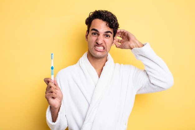 Hombre guapo joven que se siente estresado, ansioso o asustado con las manos en la cabeza, albornoz y concepto de cepillo de dientes